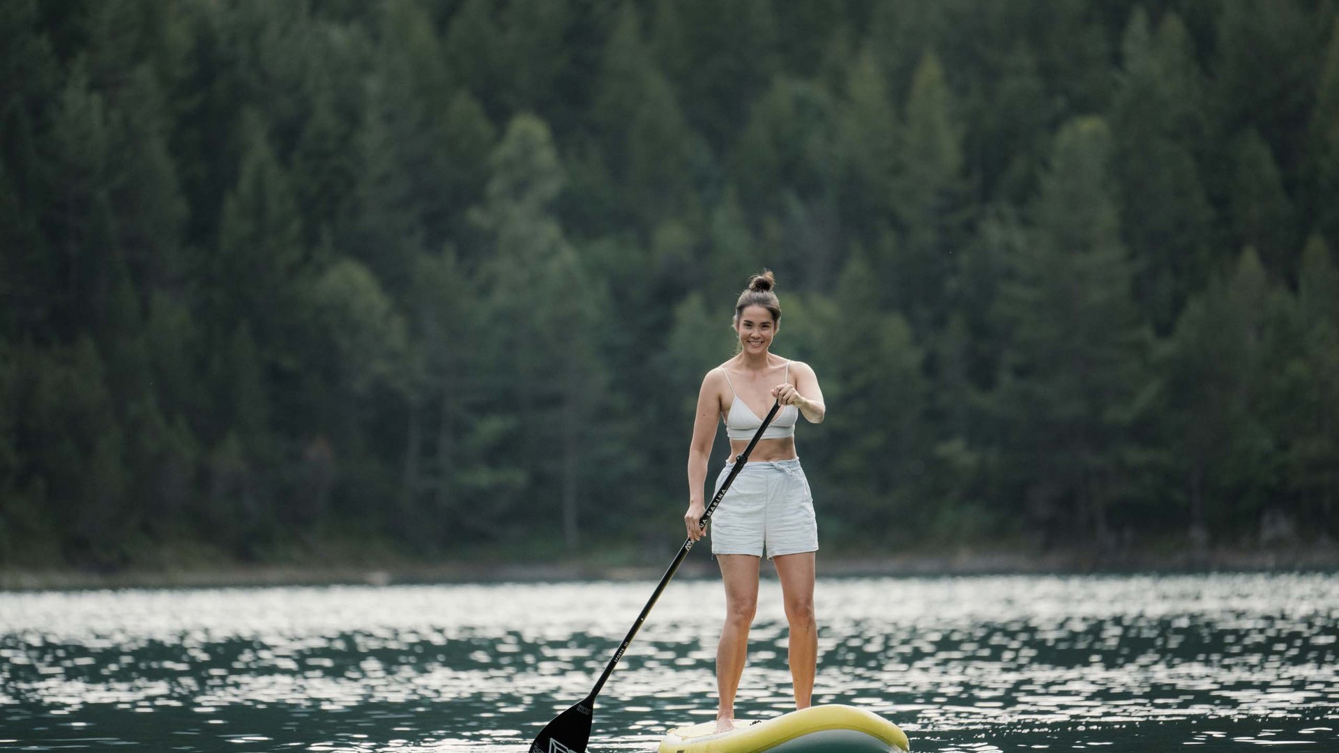 MOHR life resort Bildergalerie Frau steht auf Stand-Up-Paddleboard auf See vor Waldkulisse