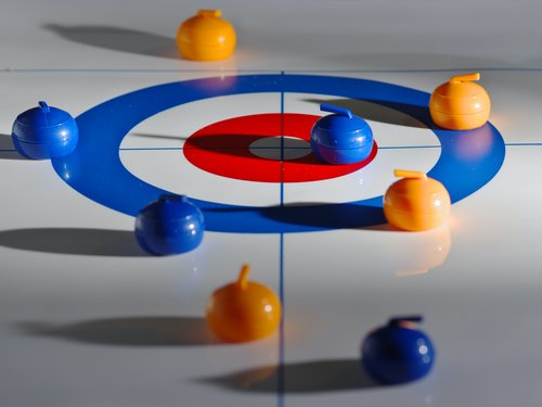 Winterurlaub in Lermoos auf dem Eis Spielsteine auf einem Curling-Spielfeld in Orange und Blau