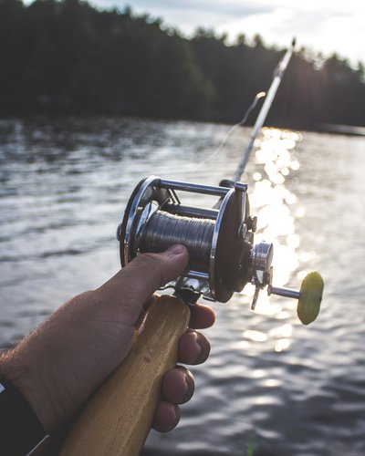 Wellness und Luxus: Ihr Hotel in Tirol Hand hält Angelrute über See mit Wald im Hintergrund