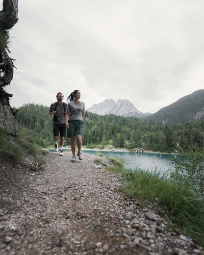 Wellness und Luxus: Ihr Hotel in Tirol Zwei Menschen wandern an einem See mit Bergen im Hintergrund