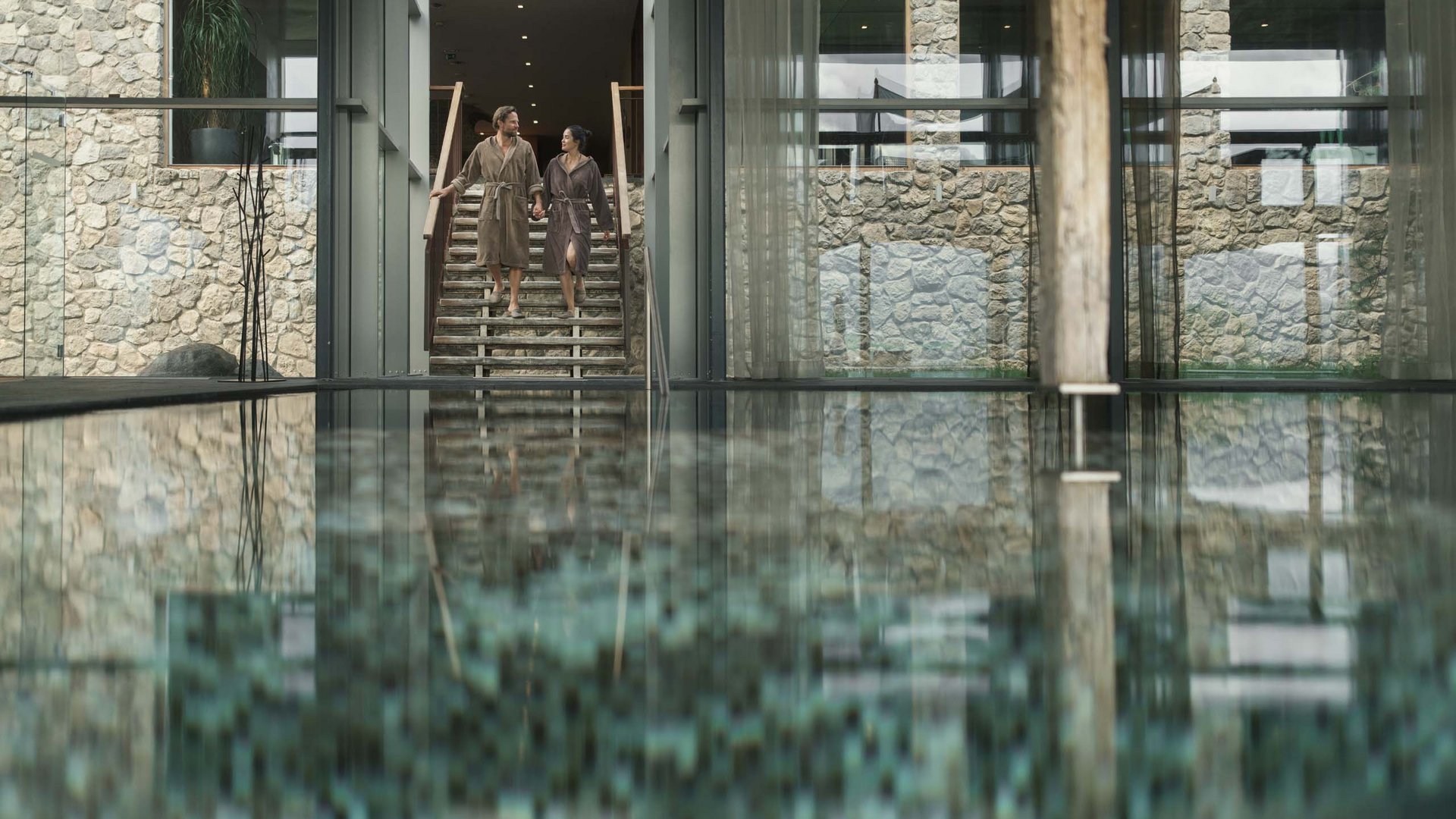 MOHR life resort Bildergalerie Paar in Bademänteln geht eine Treppe neben einem Innenpool in einem Spa