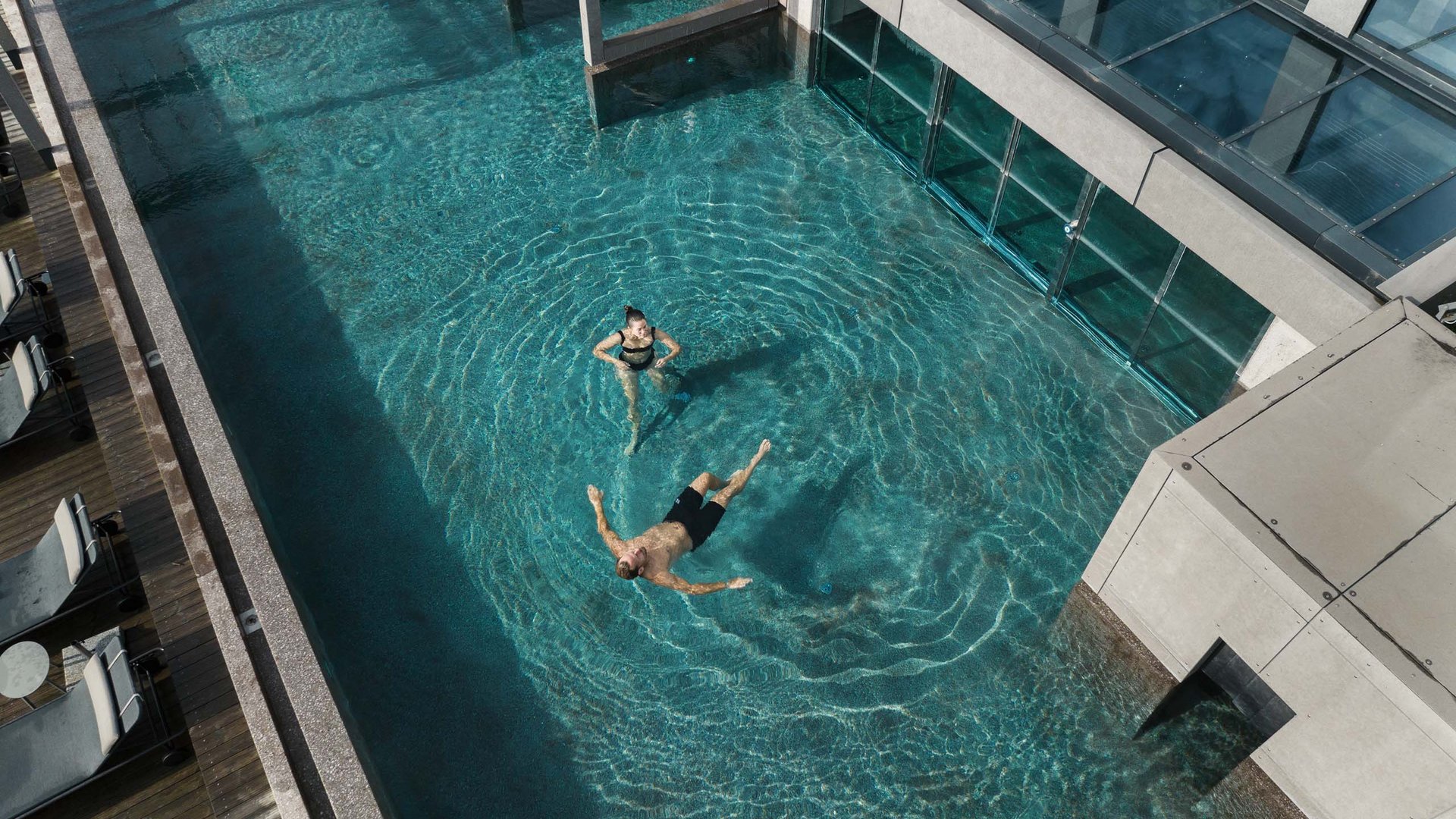 MOHR life resort Bildergalerie Personen entspannen im klaren Pool neben einem modernen Gebäude