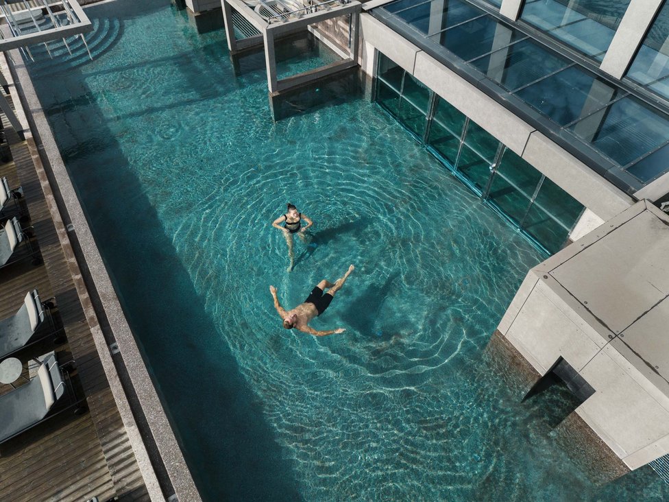 Großzügig und exklusiv: Ihr Wellnessurlaub in Tirol Personen entspannen im klaren Pool neben einem modernen Gebäude