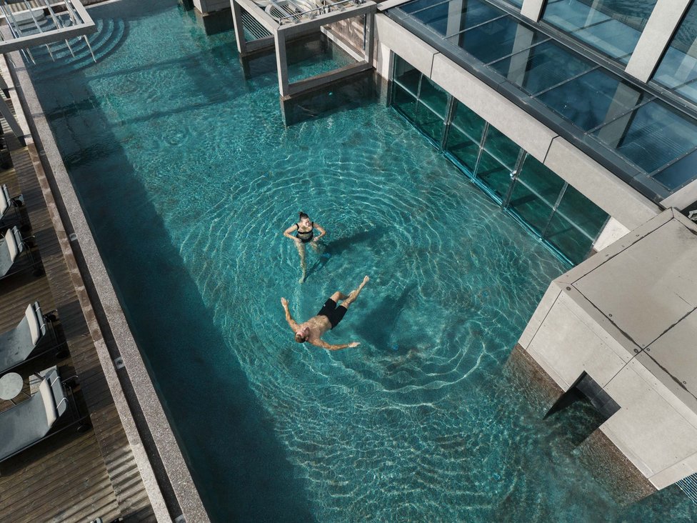 Großzügig und exklusiv: Ihr Wellnessurlaub in Tirol Personen entspannen im klaren Pool neben einem modernen Gebäude