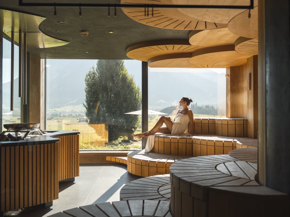Wellness und Luxus: Ihr Hotel in Tirol Frau entspannt in moderner Sauna mit großem Fenster und Bergblick