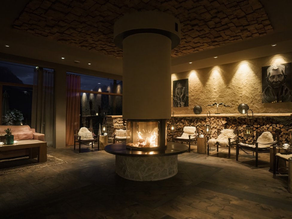Wellness und Luxus: Ihr Hotel in Tirol Gemütlicher Raum mit zentralem Kamin, Sesseln und Wandkunst bei gedämpftem Licht