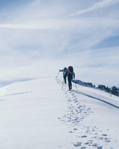 Wandern in Lermoos, Sommer wie Winter Zwei Wanderer steigen mit Stöcken auf eine schneebedeckte Bergspitze bei blauem Himmel