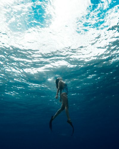 Wellness und Luxus: Ihr Hotel in Tirol Taucher mit Flossen schwimmt unter Wasser zum hellen Wasserspiegel