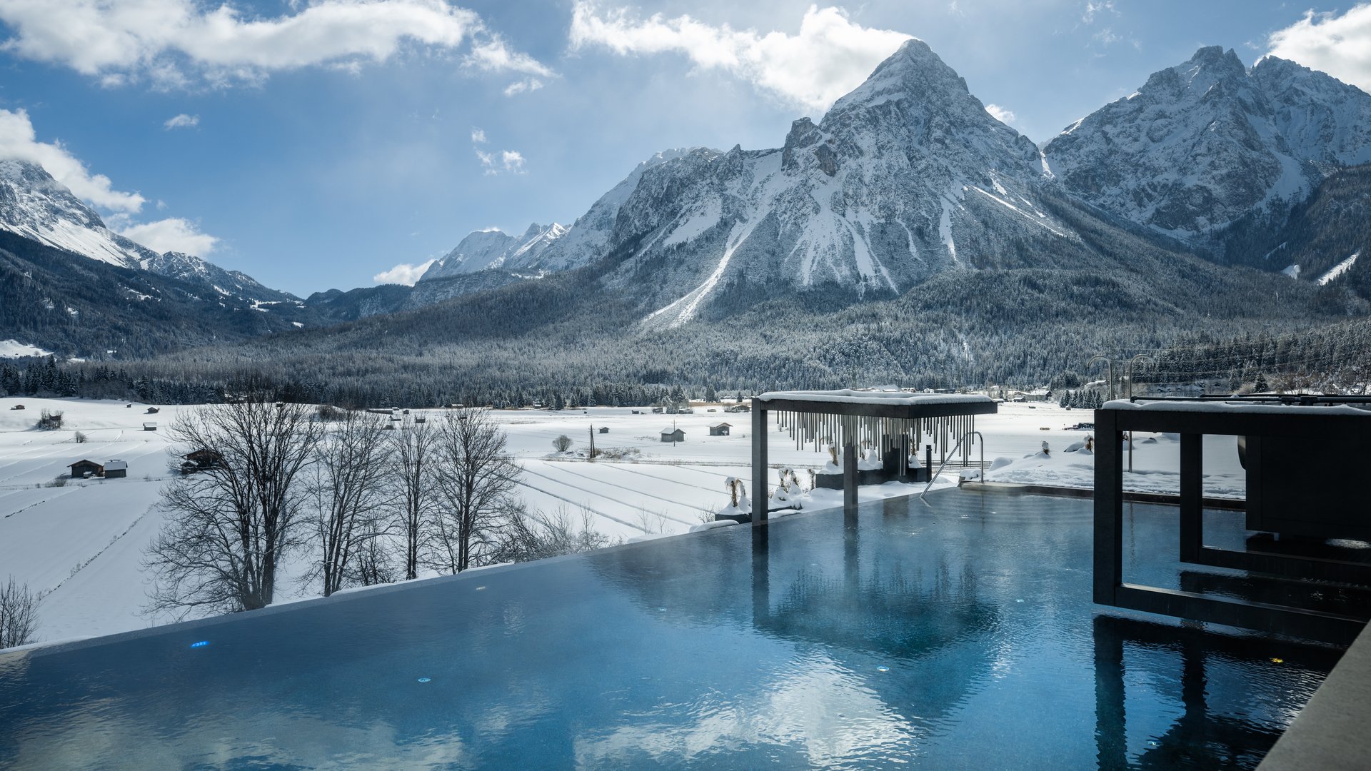 Wellness und Luxus: Ihr Hotel in Tirol Infinity-Pool mit Blick auf schneebedeckte Berge und Sommerhütten