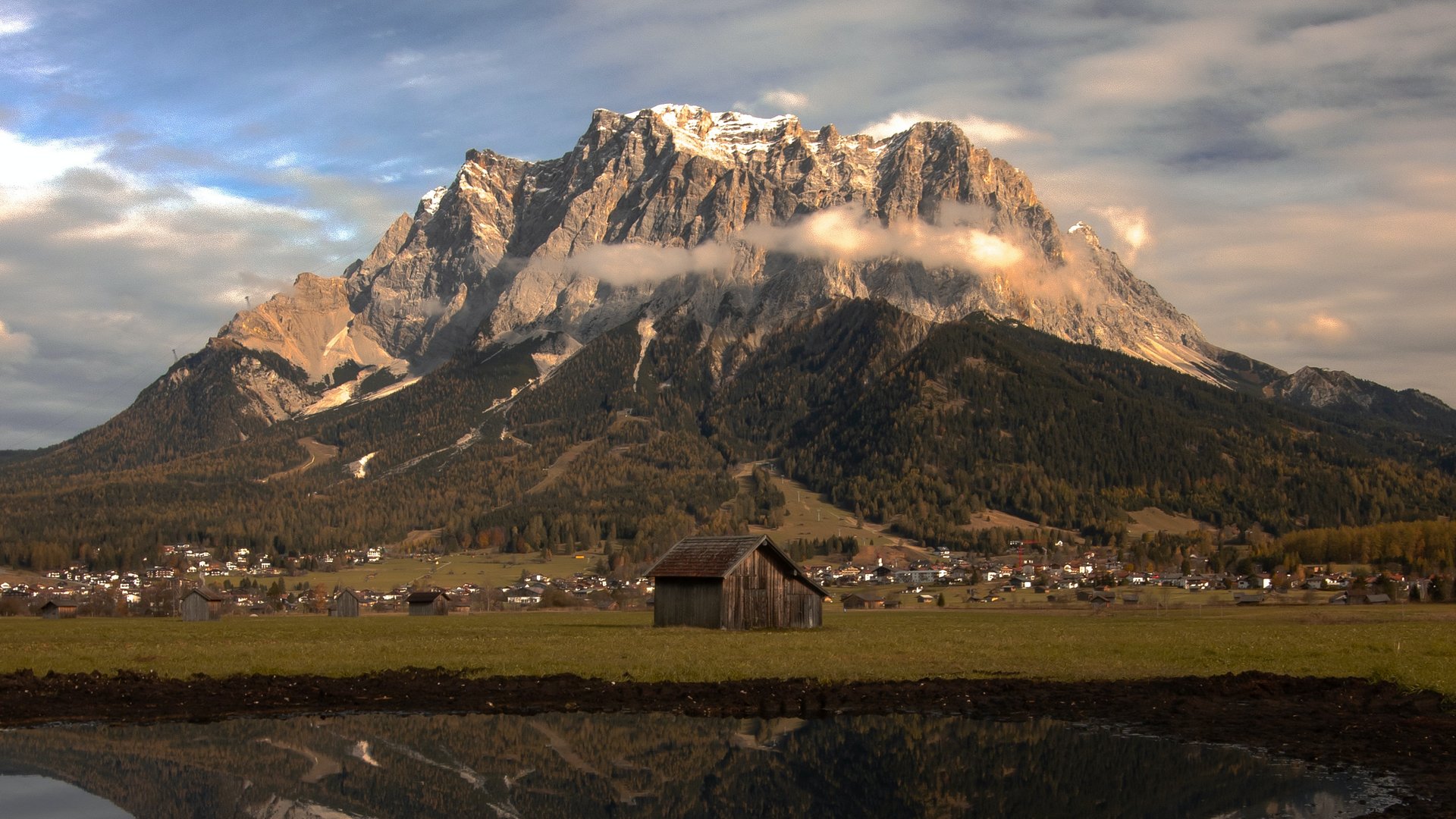 Wandern in Lermoos, Sommer wie Winter Berg mit Wolken und Spiegelung im Wasser vor einer Hütte und Dorf