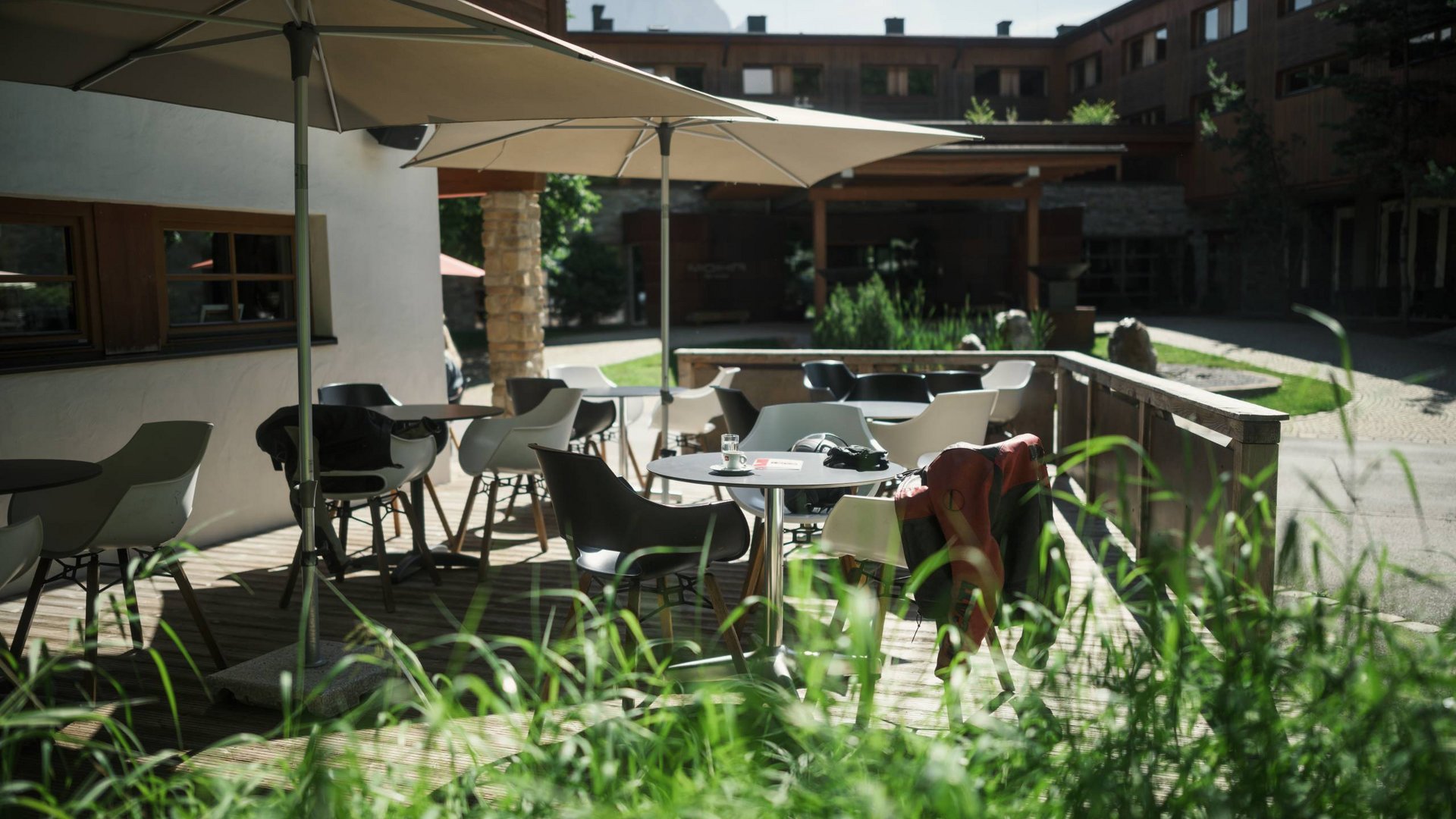 MOHR life resort Bildergalerie Sitzbereich im Freien mit Tischen, Stühlen und Sonnenschirmen vor einem Gebäude