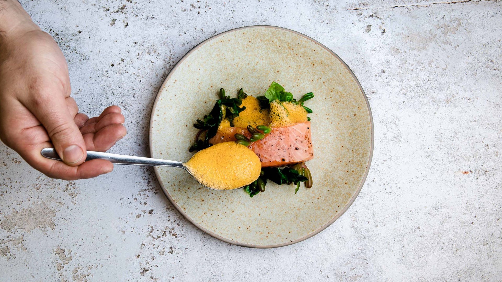 MOHR life resort Bildergalerie Hand gibt Löffel mit Sauce über Lachs und Gemüse auf Teller