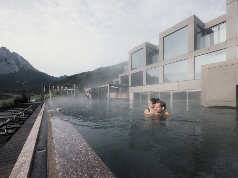 Großzügig und exklusiv: Ihr Wellnessurlaub in Tirol Paar entspannt im beheizten Außenpool eines modernen Wellnesshotels mit Bergblick