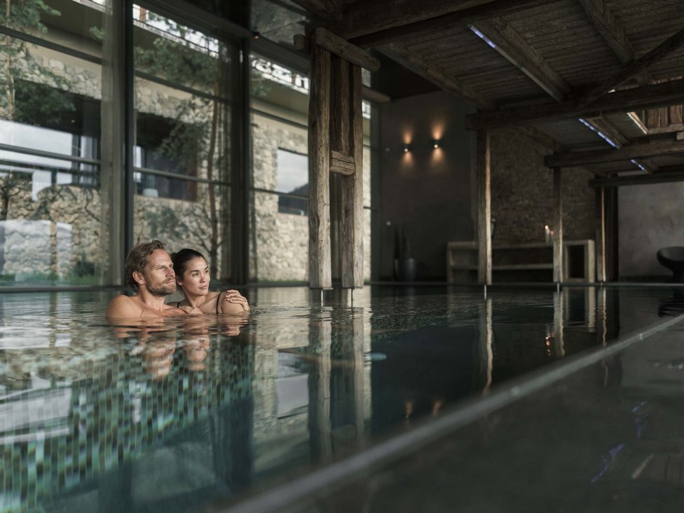 Wellness und Luxus: Ihr Hotel in Tirol Paar entspannt in einem modernen Innenpool mit Holz- und Steindekor