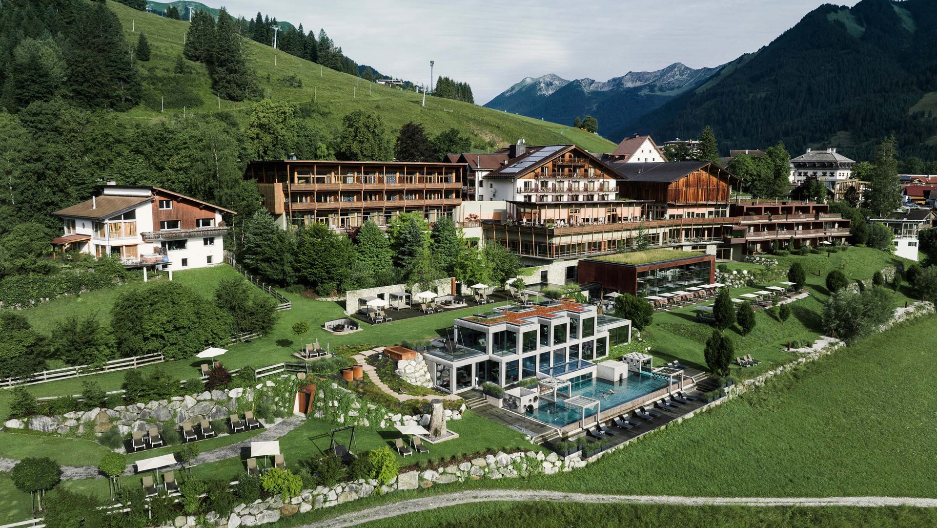 Wellness und Luxus: Ihr Hotel in Tirol Großes Hotelresort mit Garten und Pool in den Bergen bei bewölktem Himmel