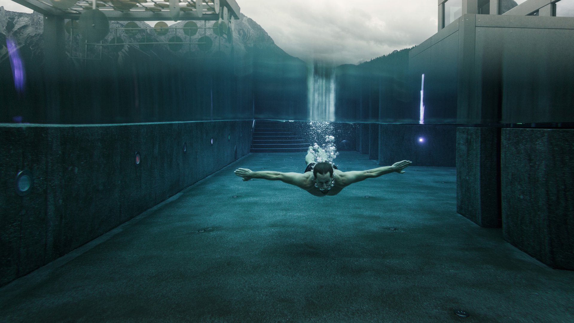 Wellness und Luxus: Ihr Hotel in Tirol Mann schwimmt unter Wasser in modernem Schwimmbecken mit Bergblick