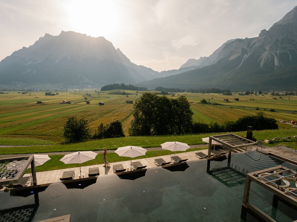 Wellness und Luxus: Ihr Hotel in Tirol Pool mit Liegestühlen und Sonnenschirmen vor Berglandschaft im Sonnenlicht