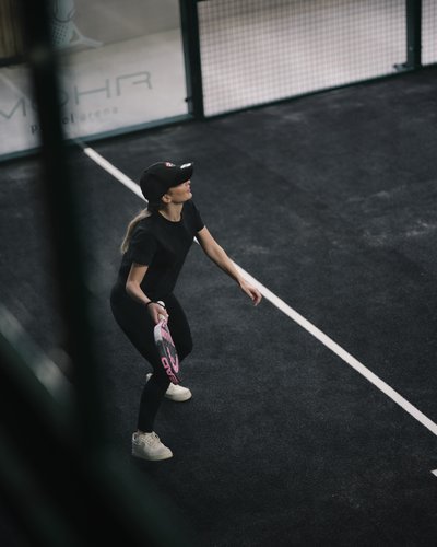 Endlich Indoor Padel spielen in Lermoos in Tirol. Im MOHR life resort Frau spielt Paddle-Tennis auf einem schwarzen Sportplatz mit Schläger und Mütze