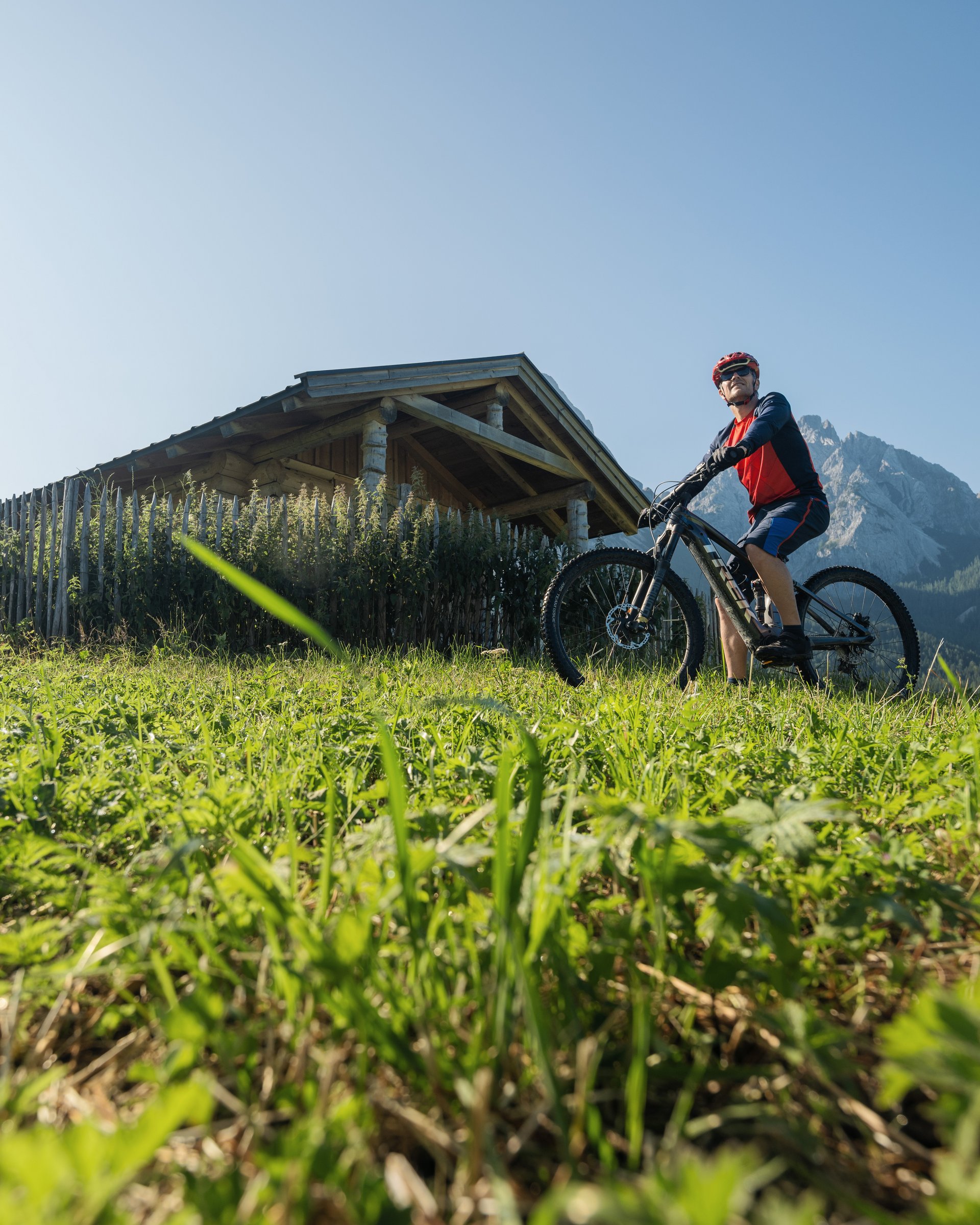 Auf Tour mit MOHR Mann mit Mountainbike vor Holzhütte und Berglandschaft an sonnigem Tag