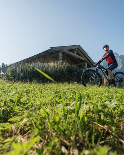 Wellness und Luxus: Ihr Hotel in Tirol Mann mit Mountainbike vor Holzhütte und Berglandschaft an sonnigem Tag