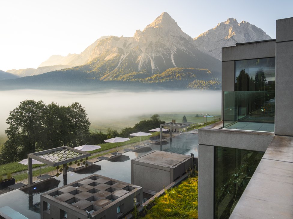Wellness und Luxus: Ihr Hotel in Tirol Blick auf Berglandschaft mit Nebel und modernem Hotelpool im Vordergrund