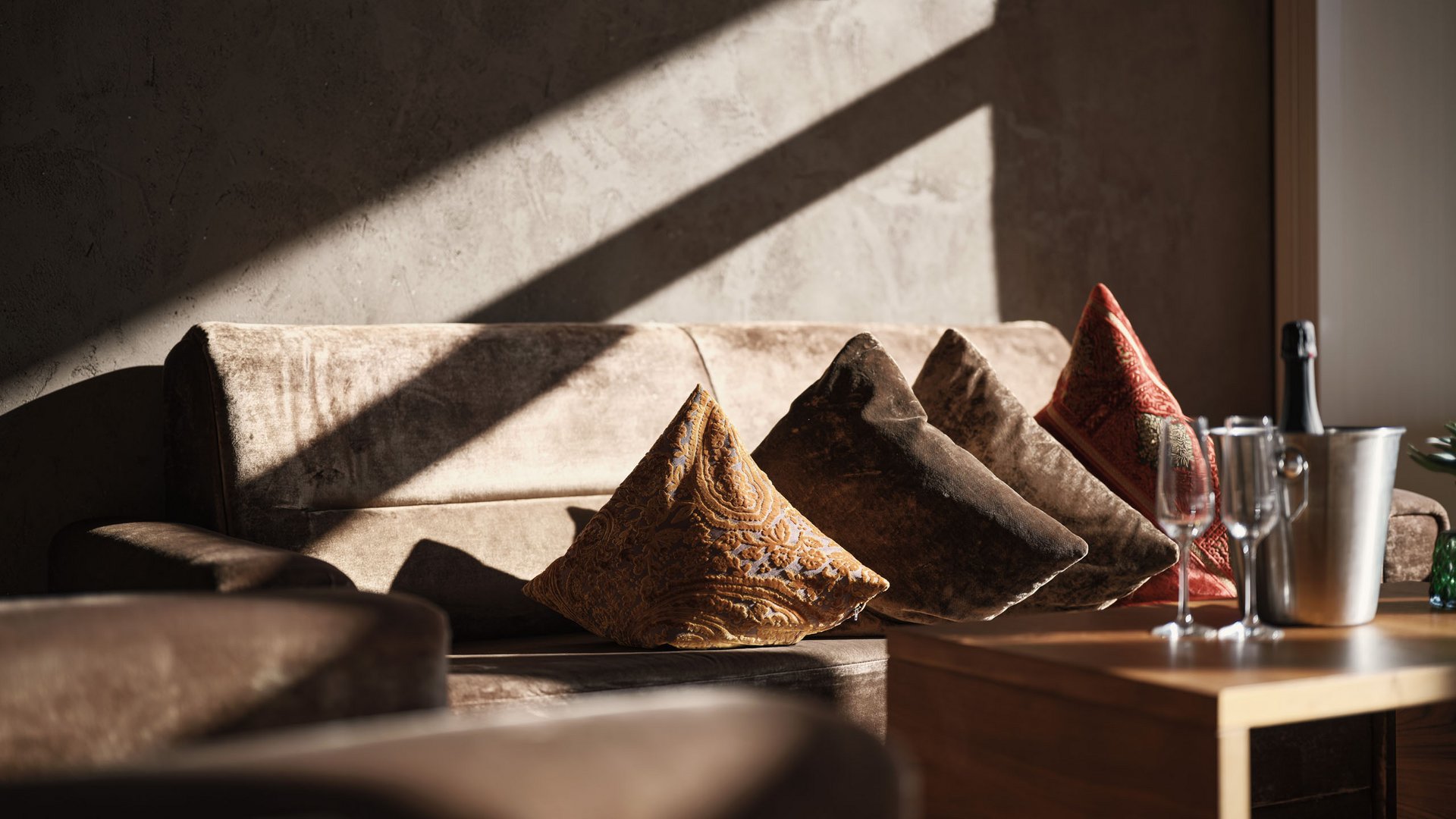 MOHR life resort Bildergalerie Sofa mit bunten Kissen und Champagner auf Holztisch im Sonnenlicht
