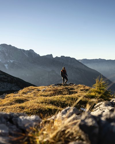 DAS Wellnesshotel am Fuß der Zugspitze Österreich Wanderer steht auf sonnenbeschienener Bergwiese mit Alpen im Hintergrund