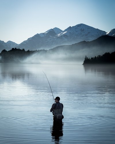 Wellness und Luxus: Ihr Hotel in Tirol Angler steht im ruhigen See vor schneebedeckten Bergen bei Morgennebel