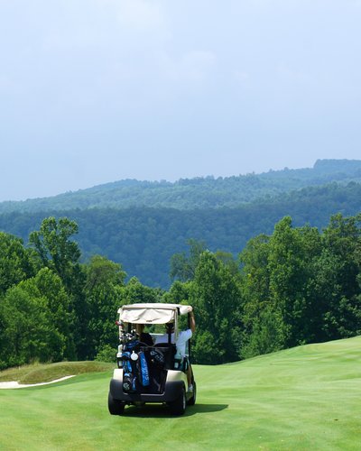 Wellness und Luxus: Ihr Hotel in Tirol Golfwagen fährt auf grünem Golfplatz vor bewaldeten Hügeln