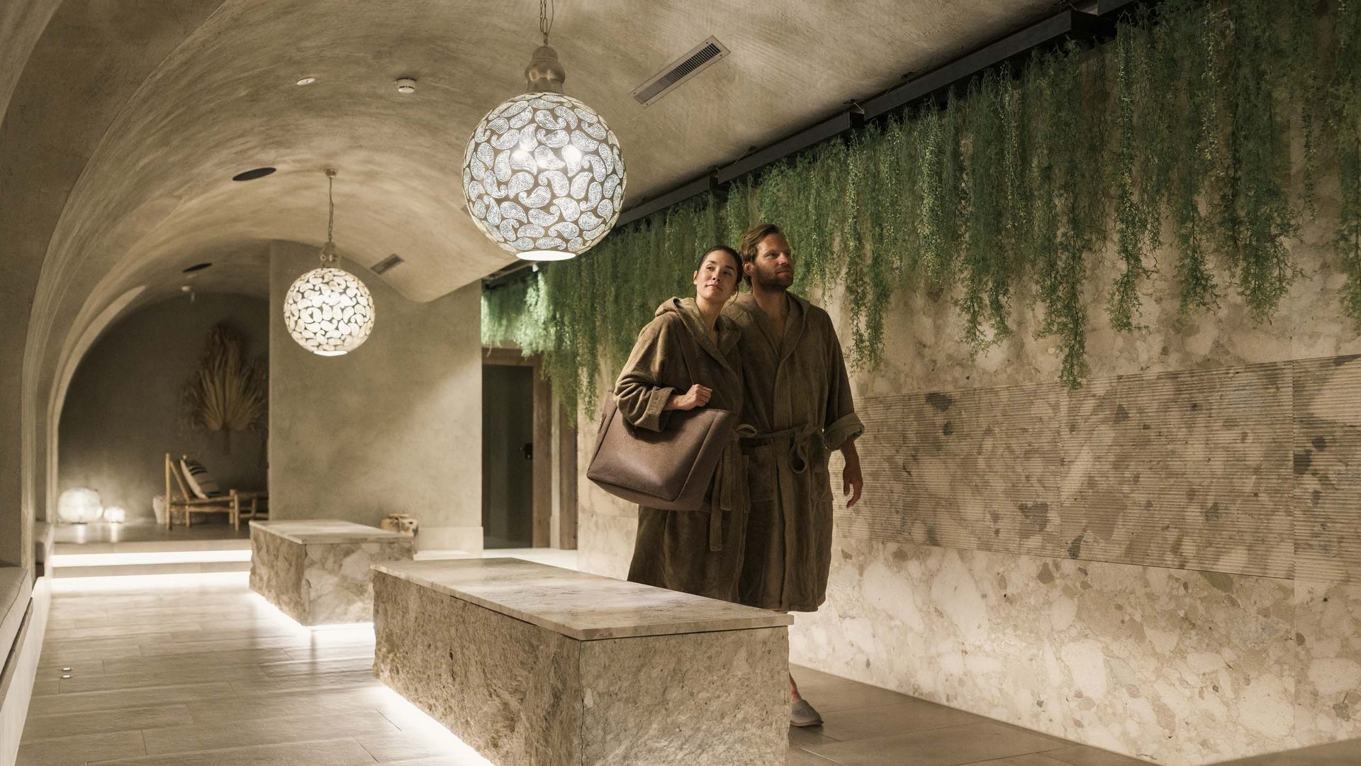 MOHR life resort Bildergalerie Paar in Bademänteln in einem stilvollen Spa-Flur mit grünen Pflanzen und Beleuchtung