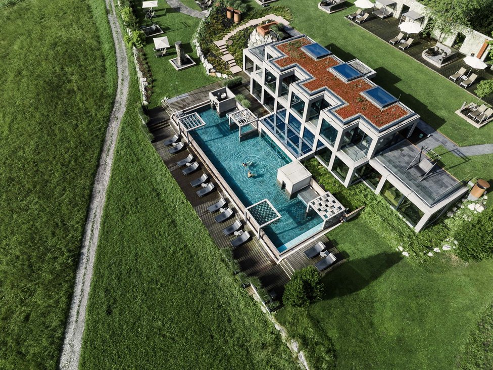 Großzügig und exklusiv: Ihr Wellnessurlaub in Tirol Moderner Wellnessbereich mit Außenpool vor einem Hotel in grüner Landschaft