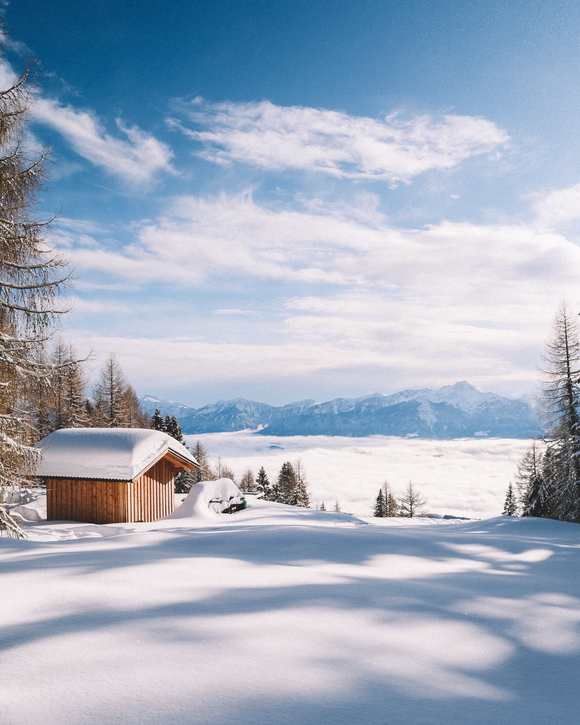 Rodeln in Lermoos – macht Spaß! Schneebedecktes Holzhaus in winterlicher Berglandschaft mit blauem Himmel