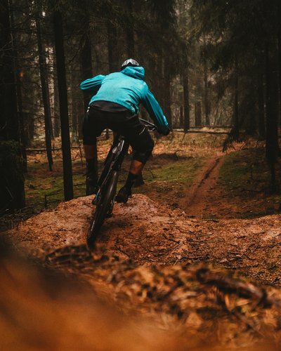 Wellness und Luxus: Ihr Hotel in Tirol Mountainbiker in blauer Jacke fährt im Wald auf einem schmalen Pfad