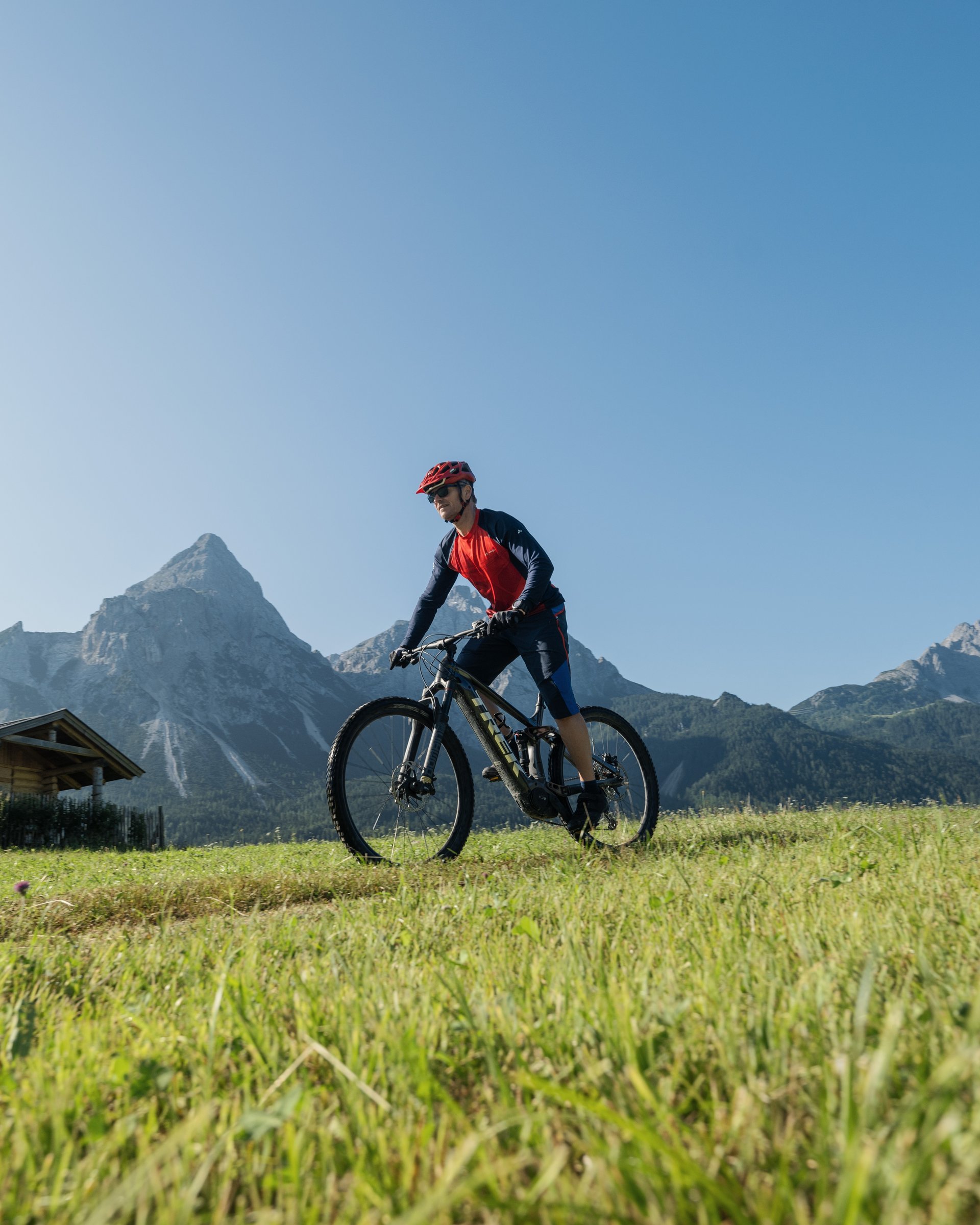 MOHR bedeutet mehr Bike-Urlaub in Tirol Mann fährt Mountainbike auf einer Wiese mit Bergkulisse bei klarem Himmel