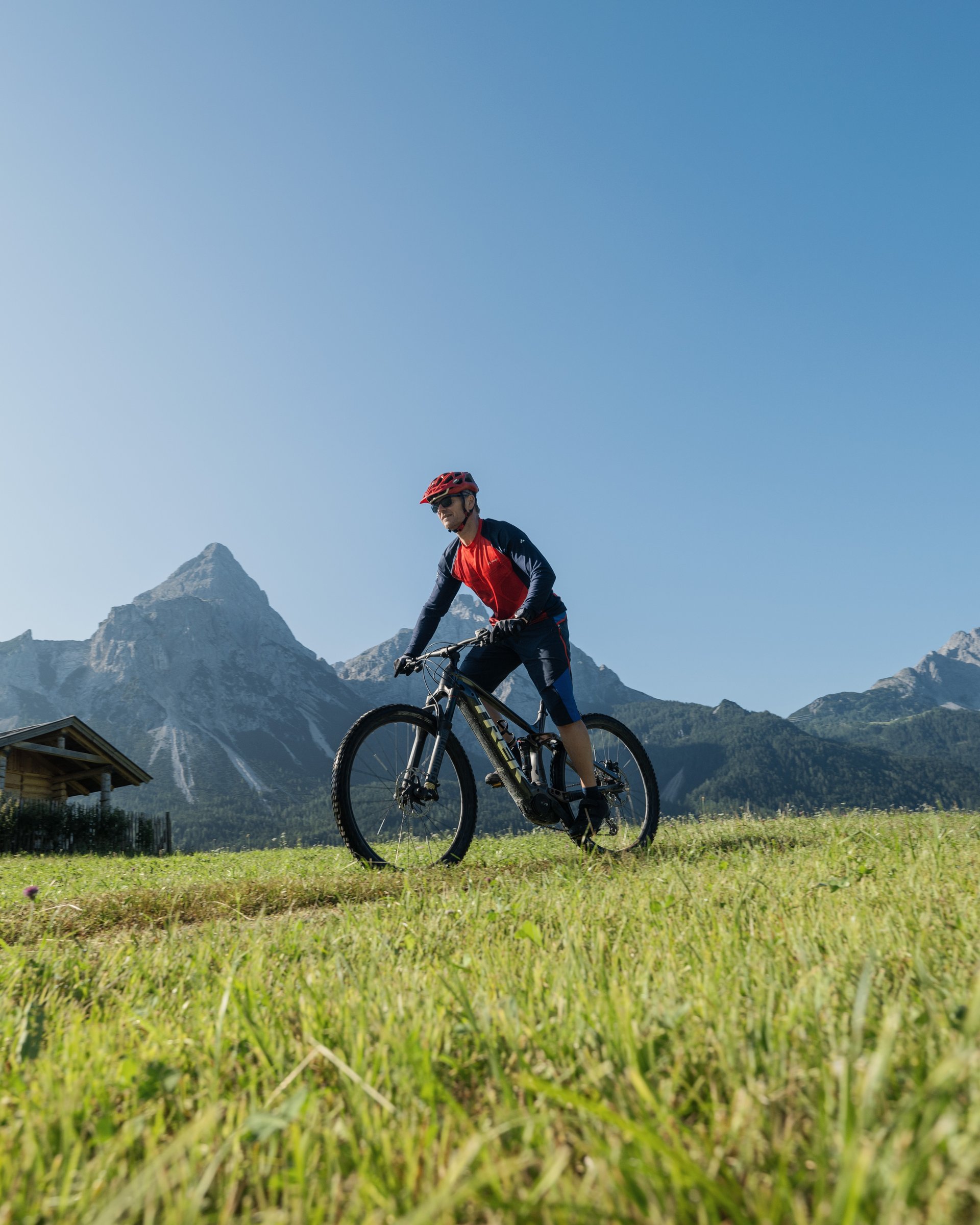 Aktivurlaub in Lermoos in Österreich Mann fährt Mountainbike auf einer Wiese mit Bergkulisse bei klarem Himmel