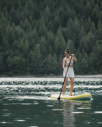 Wellness und Luxus: Ihr Hotel in Tirol Frau paddelt auf einem Stand-Up-Paddle-Board auf einem See mit Waldblick