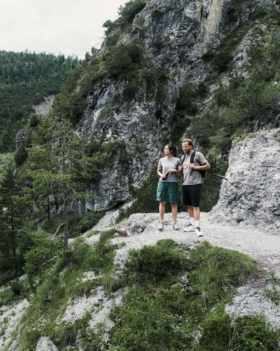 Bereit für MOHR? Das Sporthotel in Lermoos Zwei Wanderer stehen auf einem Felsen mit Blick auf einen Bergsee und Wald