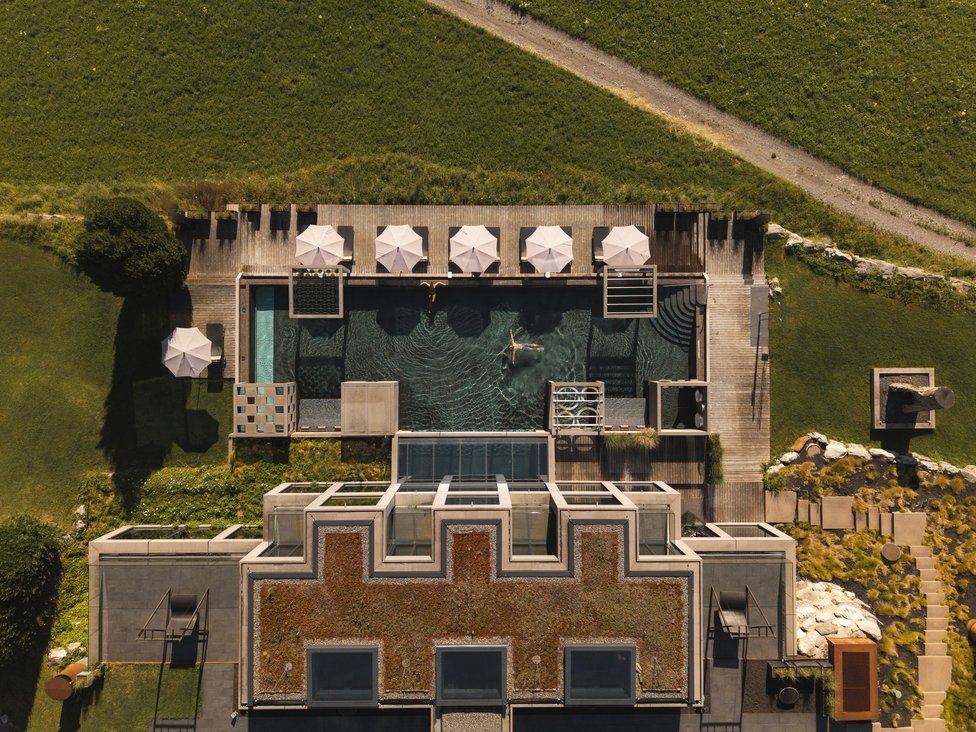 Wellness und Luxus: Ihr Hotel in Tirol Vogelperspektive auf Pool mit Sonnenschirmen und zwei Schwimmern neben modernem Gebäude
