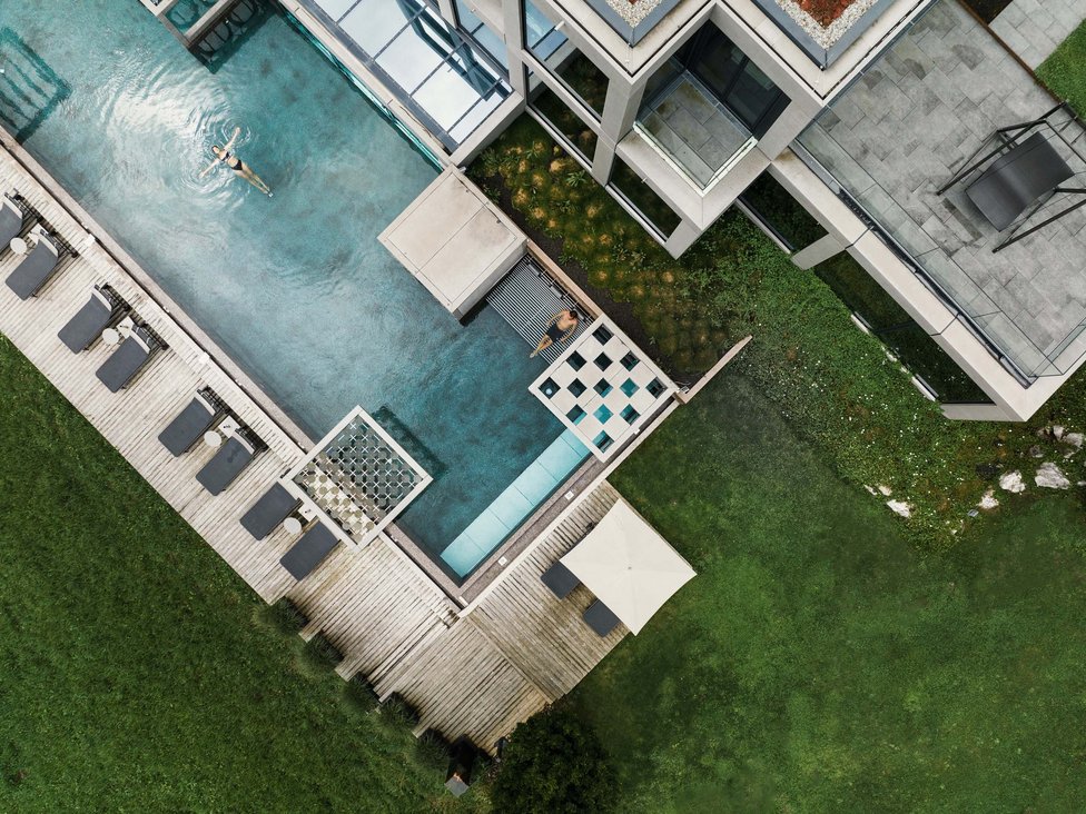 Großzügig und exklusiv: Ihr Wellnessurlaub in Tirol Vogelperspektive auf Pool mit zwei Personen und Liegestühlen an einem modernen Gebäude