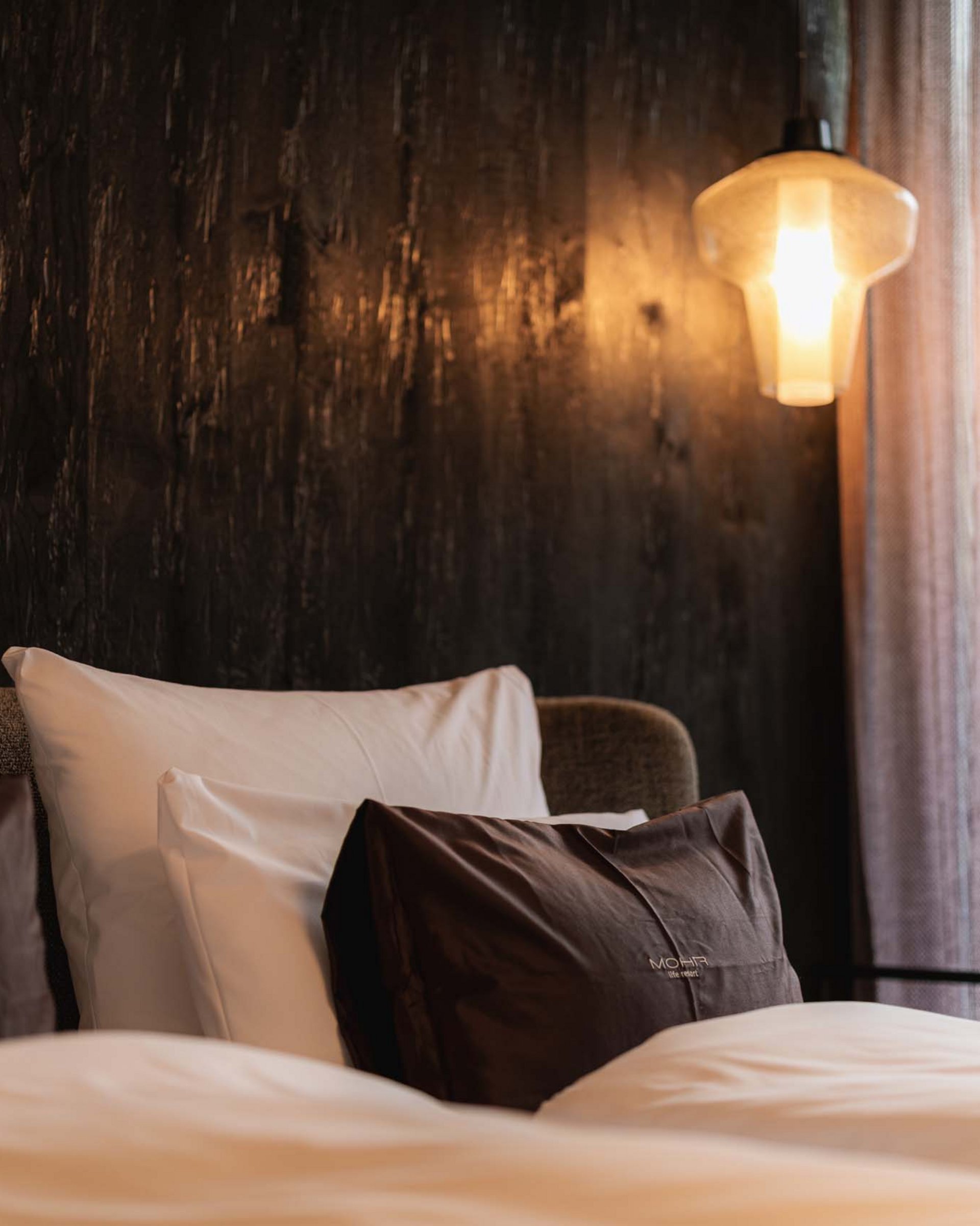 Wandern in und rund um Lermoos Gemütliches Doppelbett mit braunen und weißen Kissen, warme Beleuchtung