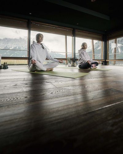 Wellness und Luxus: Ihr Hotel in Tirol Zwei Frauen meditieren auf Yoga-Matten in einem Raum mit Bergblick