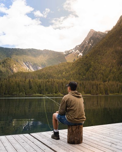 Wellness und Luxus: Ihr Hotel in Tirol Mann sitzt am Steg und angelt in einem Bergsee vor bewaldeten Bergen