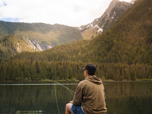 Sehenswürdigkeiten rund um Lermoos Mann sitzt am Steg und angelt in einem Bergsee vor bewaldeten Bergen