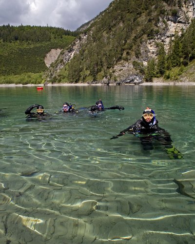 Wellness und Luxus: Ihr Hotel in Tirol Vier Taucher im klaren Bergsee vor bewaldetem Felsen