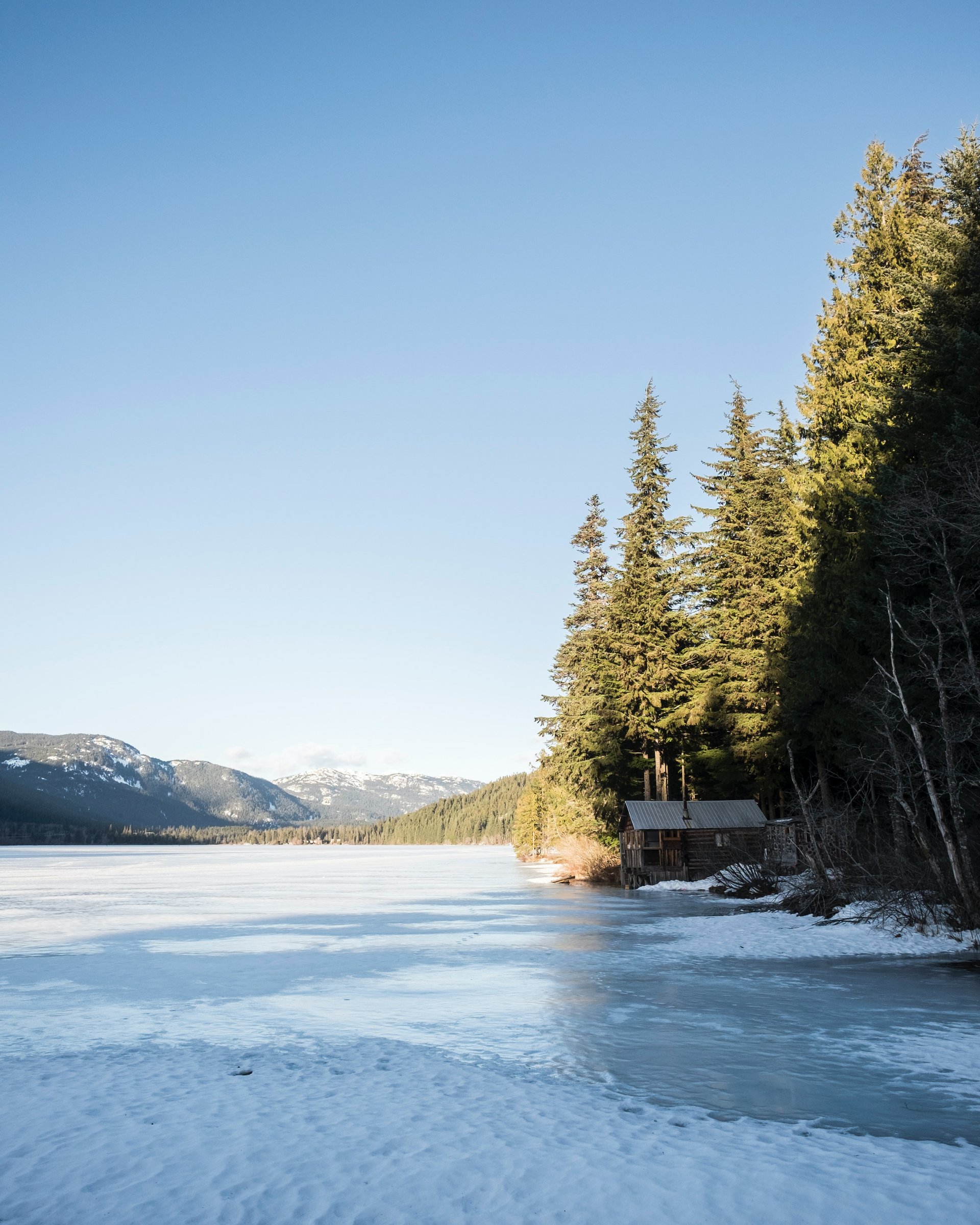 Winterurlaub in Lermoos auf dem Eis Vereister See mit verschneiter Hütte und Tannen im Sonnenschein