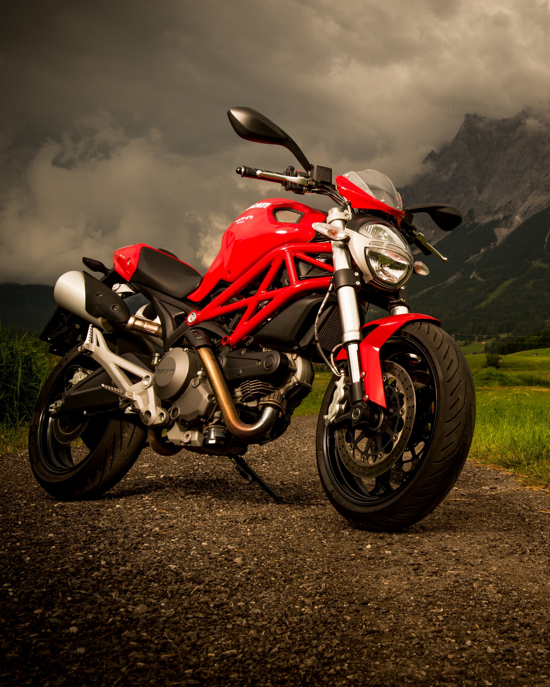 Auf Tour mit MOHR Rotes Motorrad auf Landstraße mit Berg und wolkigem Himmel im Hintergrund