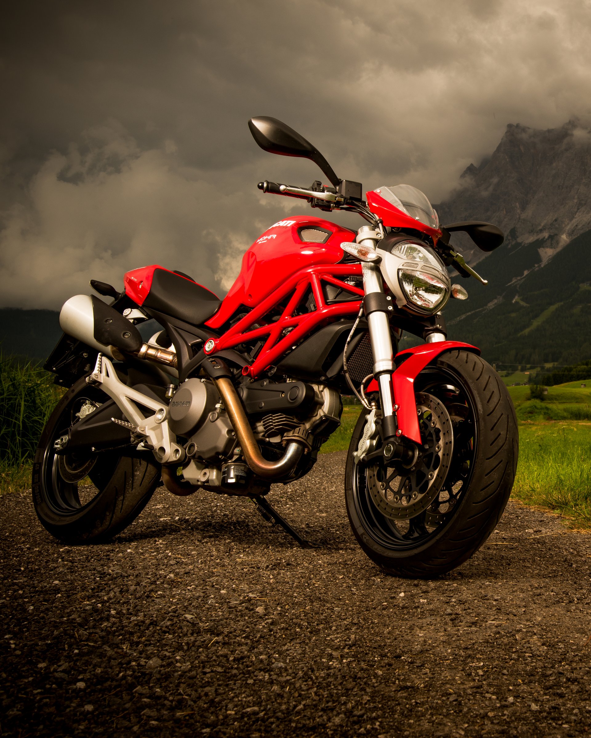Tour de MOHR Rotes Motorrad auf Landstraße mit Berg und wolkigem Himmel im Hintergrund
