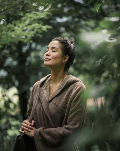 MOHR life resort – Nachhaltigkeit im Hotel in Tirol Frau in braunem Bademantel entspannt sich draußen mit geschlossenen Augen