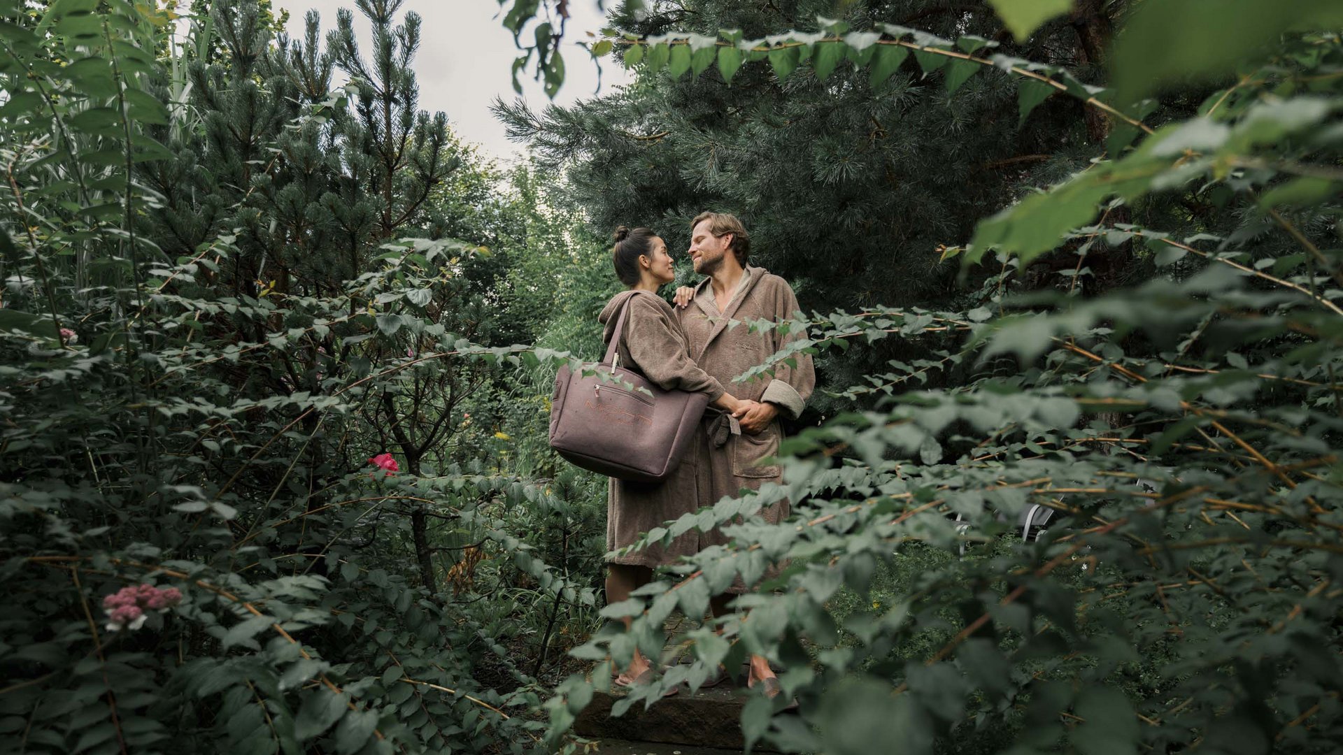 Großzügig und exklusiv: Ihr Wellnessurlaub in Tirol Paar in Bademänteln umgeben von Bäumen und Pflanzen im Garten