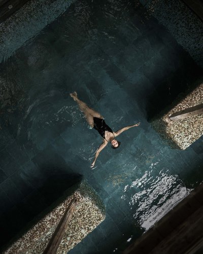 Ihr Favorit? MOHR life resort – das Hotel in Lermoos Frau schwimmt entspannt auf dem Rücken in einem Innenpool mit Mosaikfliesen